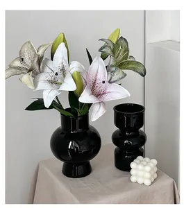 Close-up of black ceramic vases with lifelike 3D lily flowers and a bubble candle