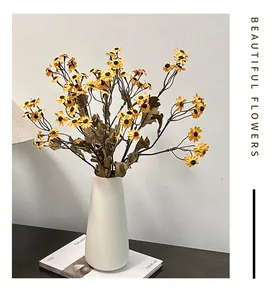 Gele kunstmatige madeliefjes in een minimalistische witte keramische vaas op tafel