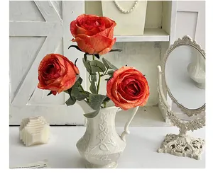 Three coral orange artificial roses in a white embossed ceramic vase for home decor
