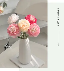 Detail of silk ranunculus bouquet in matte white ceramic vase on modern desktop