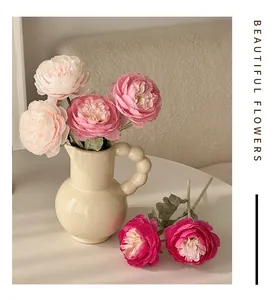Detailed view of artificial pink peonies in a cream ceramic vase with ball handles