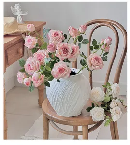 Primer plano de rosas artificiales vintage en un jarrón de cerámica blanca texturizada