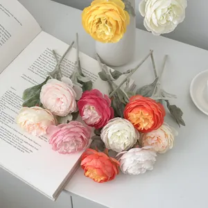 Artificial multicolor ranunculus bouquet on an open art book with a minimalist ceramic vase