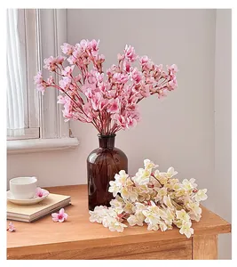 Vista detallada de flores de cerezo de seda rosa y crema en un jarrón sobre una mesa