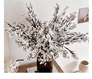White silk gypsophila artificial flowers in a dark brown glass vase on a wooden desk