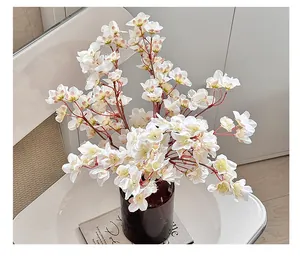 Primer plano de flores de cerezo blancas artificiales en un jarrón de vidrio marrón