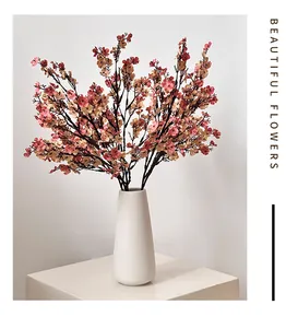 Close-up of pink silk cherry blossom stems in a white matte ceramic vase for home decor