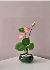 Close-up of artificial pink lotus flowers in a green ceramic pot with white stones