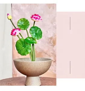 Detailed view of pink artificial lotus flowers in a rustic ceramic pot on a wooden base