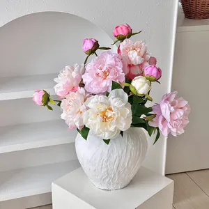 Bouquet de pivoines artificielles élégantes dans un vase blanc texturé sur socle