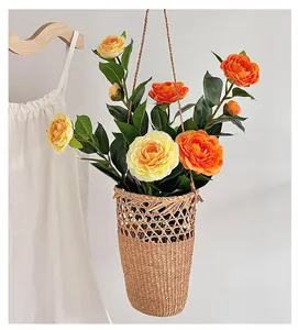 Hängender handgewebter Korb mit leuchtend orangefarbenen und gelben Kunst-Kamelienblüten