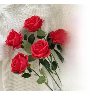 Close-up of five artificial red roses with green leaves on a white knit sweater background