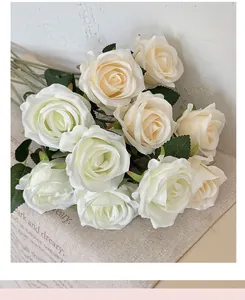 Close-up of ivory silk rose bouquet with green leaves on a linen texture background