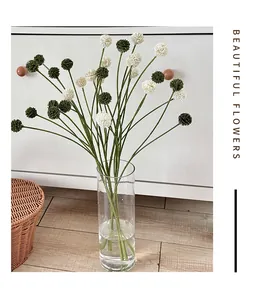 Detail van witte en groene kunstmatige pomponbloemen in een heldere glazen vaas