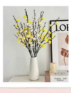 Detalle de jarrón blanco con ramas realistas de flores de ciruelo amarillas y blancas