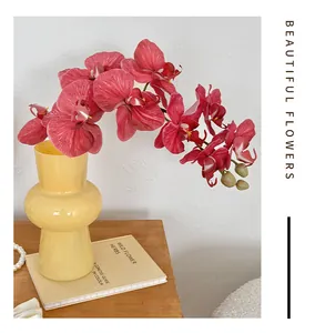 Pink artificial orchid in a modern yellow glass vase on a wooden table setup