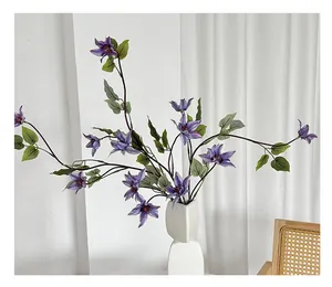 Gros plan de clématites violettes artificielles texturées dans un vase en céramique blanche