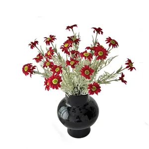 Artificial red daisy silk flowers with green leaves in a black glossy ceramic vase