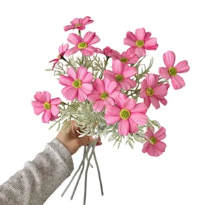 Hand hält einen Strauß rosa künstlicher Kosmosblumen vor weißem Hintergrund