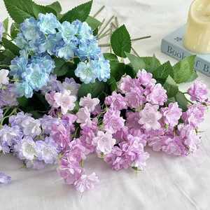 Artificial jasmine silk flowers in blue and purple on white fabric with a candle