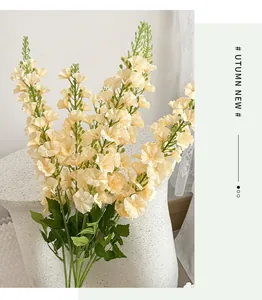 Detail of creamy yellow artificial larkspur flowers with green leaves on stone stool