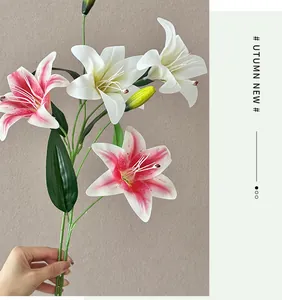 Close-up of artificial lily branch with white pink petals and green buds held by hand