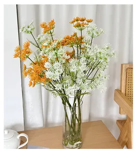 Close-up of artificial Queen Anne's lace flowers in a glass vase on a wooden table