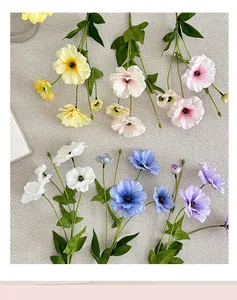 Detail view of colorful silk faux flowers with realistic petals and green leaves on fabric