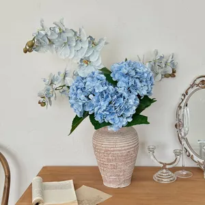 Blue artificial hydrangea and orchids in a textured ceramic vase on a wooden table