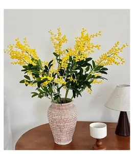 Détail de fleurs d'acacia jaunes dans un vase en céramique texturé sur un bureau en bois