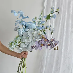 Detail of blue orchid and hydrangea bouquet with stems held against white curtains
