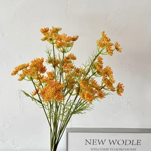 Vibrant orange lace artificial flowers with green leaves against a minimalist white wall