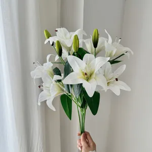 Hand holding a lifelike bouquet of white artificial lilies with buds and green leaves