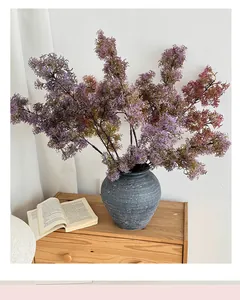 Detail of purple artificial pine branch in a grey textured ceramic vase on a wooden cabinet