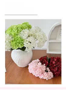 Detail of colorful artificial hydrangeas in a textured white ceramic vase on wood table