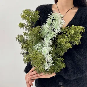 Realistic purple asparagus fern spray for home decor held by hand against white backdrop