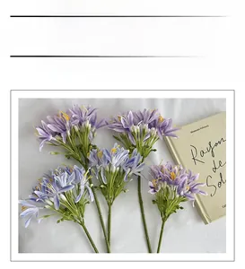Detail of five lavender faux Agapanthus stems with yellow stamens on white cloth