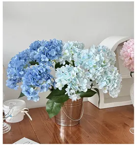 Blue and pink faux hydrangea flowers in a vintage silver metal bucket on a wooden table
