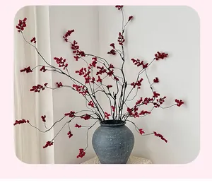 Close-up of vibrant red winterberry stems in a matte grey textured vase for home decor