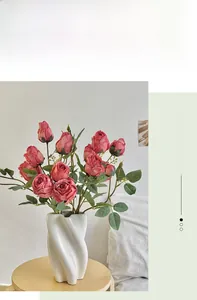 Pink faux roses in a white spiral ceramic vase on a wooden table for home decor