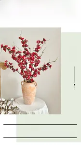 Close-up of red artificial plum blossom branches in a vintage clay vase for home decor