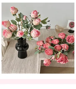 Pink silk roses in a matte black ceramic vase on a marble table with soft lighting