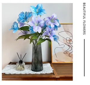 Gigli di seta blu e viola in un vaso di vetro grigio su un tavolo di legno decorato
