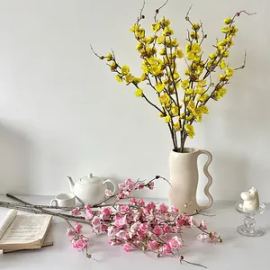 Artificial plum blossom branches in yellow and pink set in a wave-textured cream vase