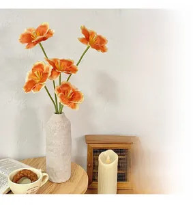 Vibrant 3D printed orange tulips in a white textured vase on a wooden table setup