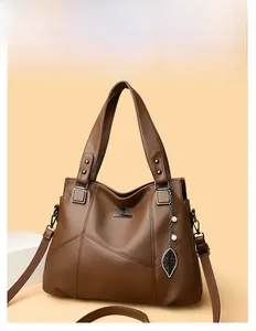 Detailed view of brown leather handbag featuring V-shaped stitching and leaf pendant