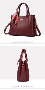 Detail of burgundy pebbled leather handbag with silk scarf and golden hardware accents