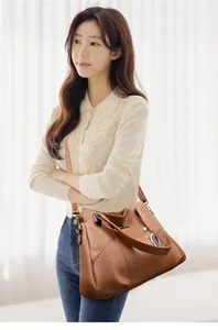 Detailed shot of a brown leather shoulder bag with gold leaf pendant and kangaroo logo