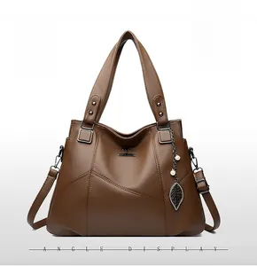 Detail view of brown pebbled leather handbag featuring pearl and leaf pendant charm