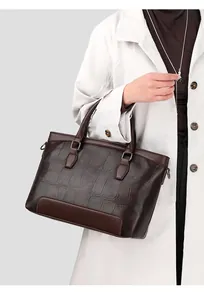 Detailed view of crocodile embossed leather handbag on model in white trench coat
